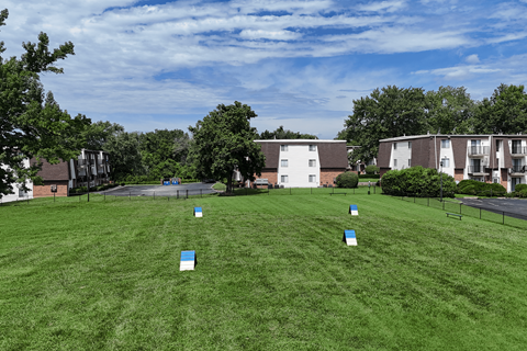 A grassy field with blue and white objects scattered around and apartment buildings in the background.