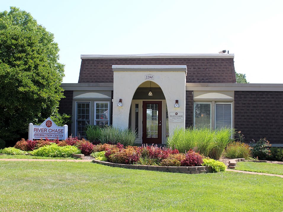 the front of the leasing office with a lawn and flowers
