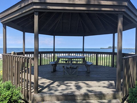 A wooden gazebo with a table and chairs overlooking the water.