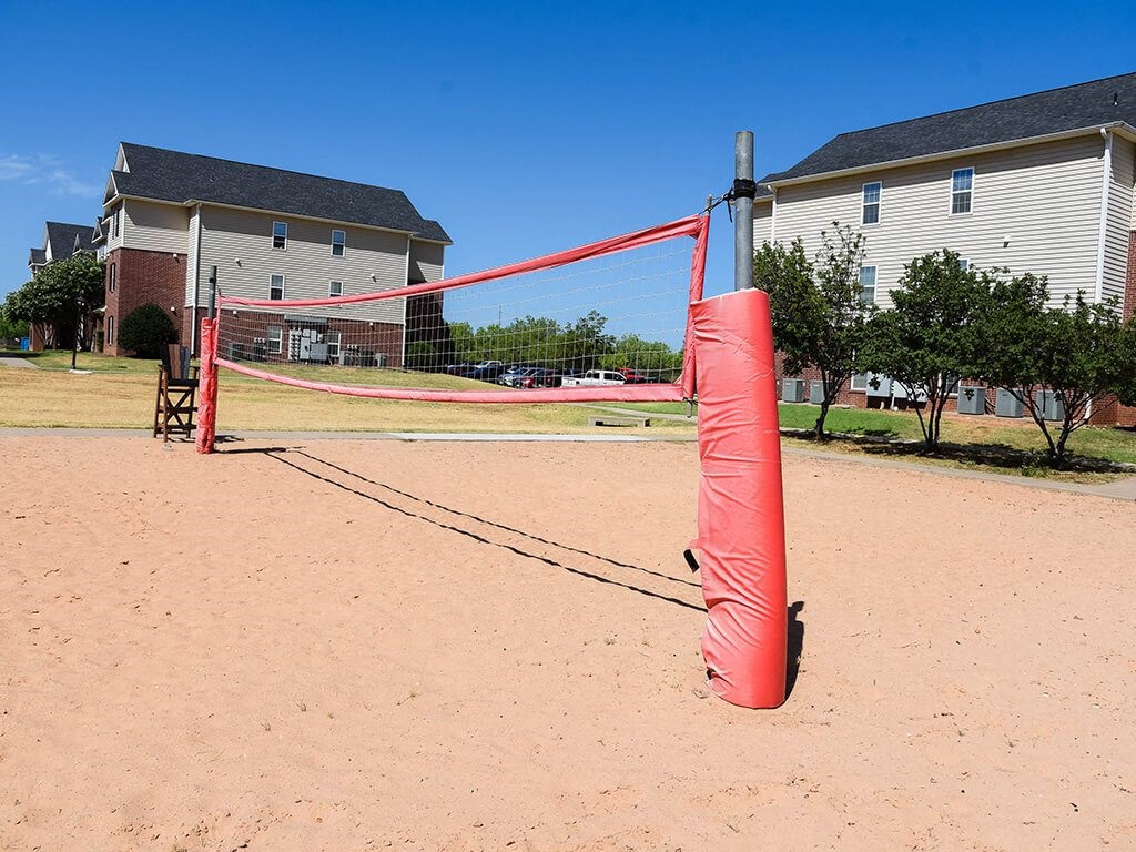 a red net on a sandy playground with houses in the background