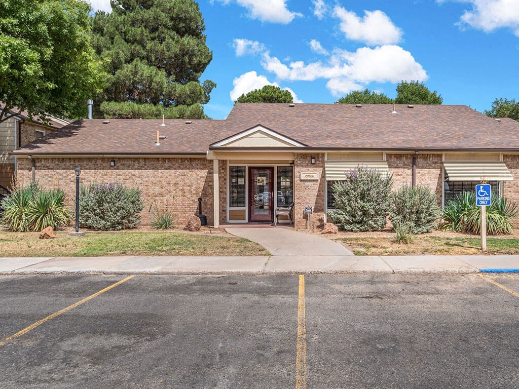 the front of a brick building with a sidewalk and a parking lot