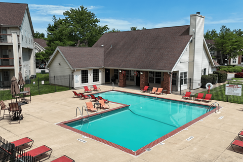 A pool with red chairs and a white house in the background.