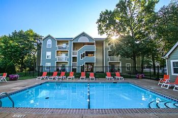 a swimming pool with red chairs and an apartment building in the background