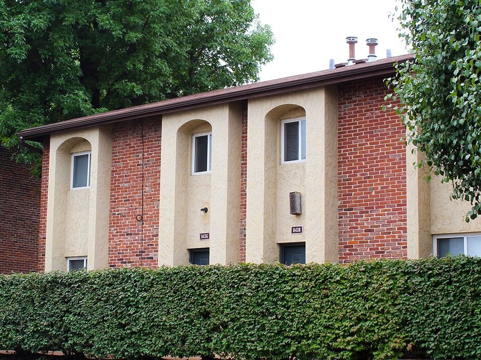 a brick building with arched windows and a hedge in front of it