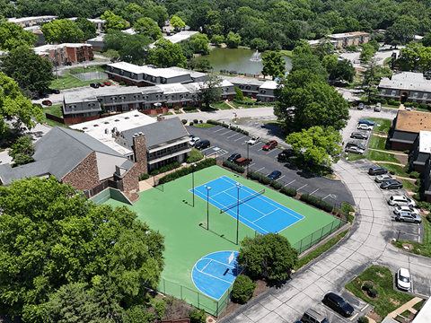 A tennis court is surrounded by a parking lot and buildings.