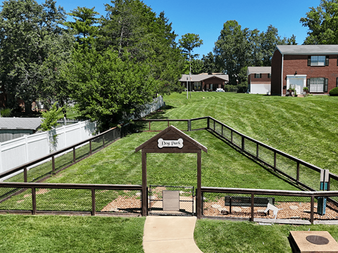 A park with a sign that says "Dog Park" in the middle of a grassy area.