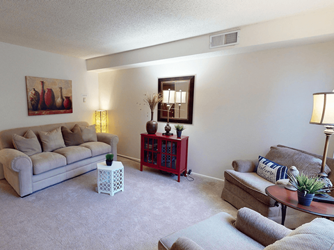 A living room with a grey couch, a red side table, and a painting on the wall.