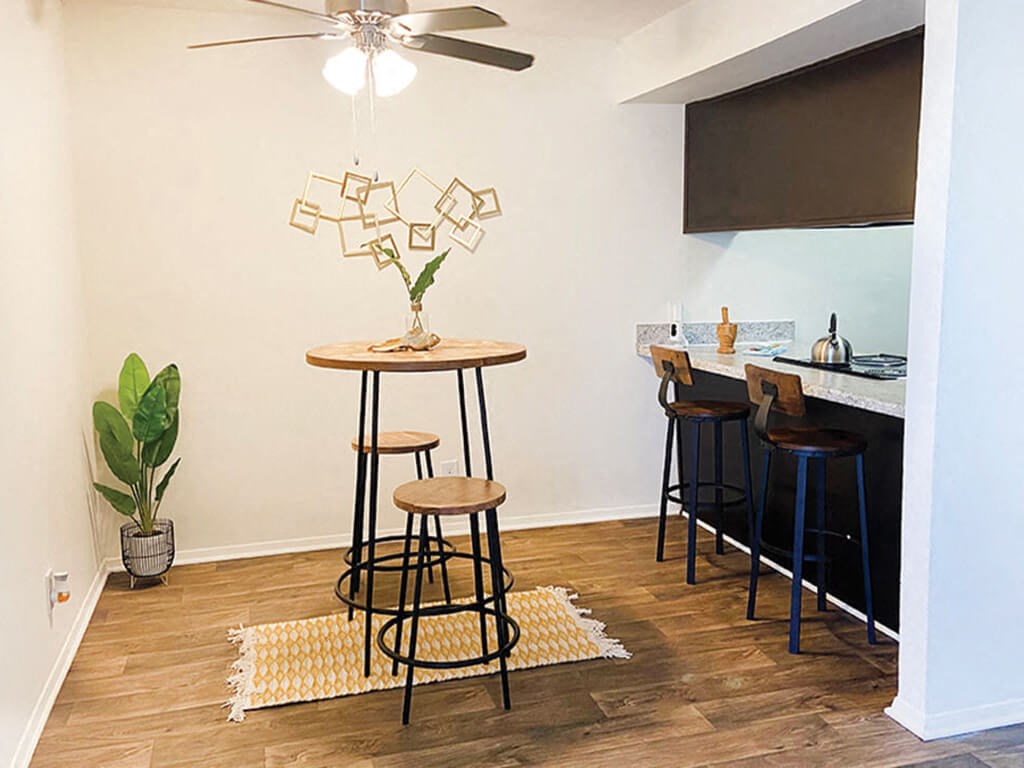 a living room with a bar with stools and a ceiling fan