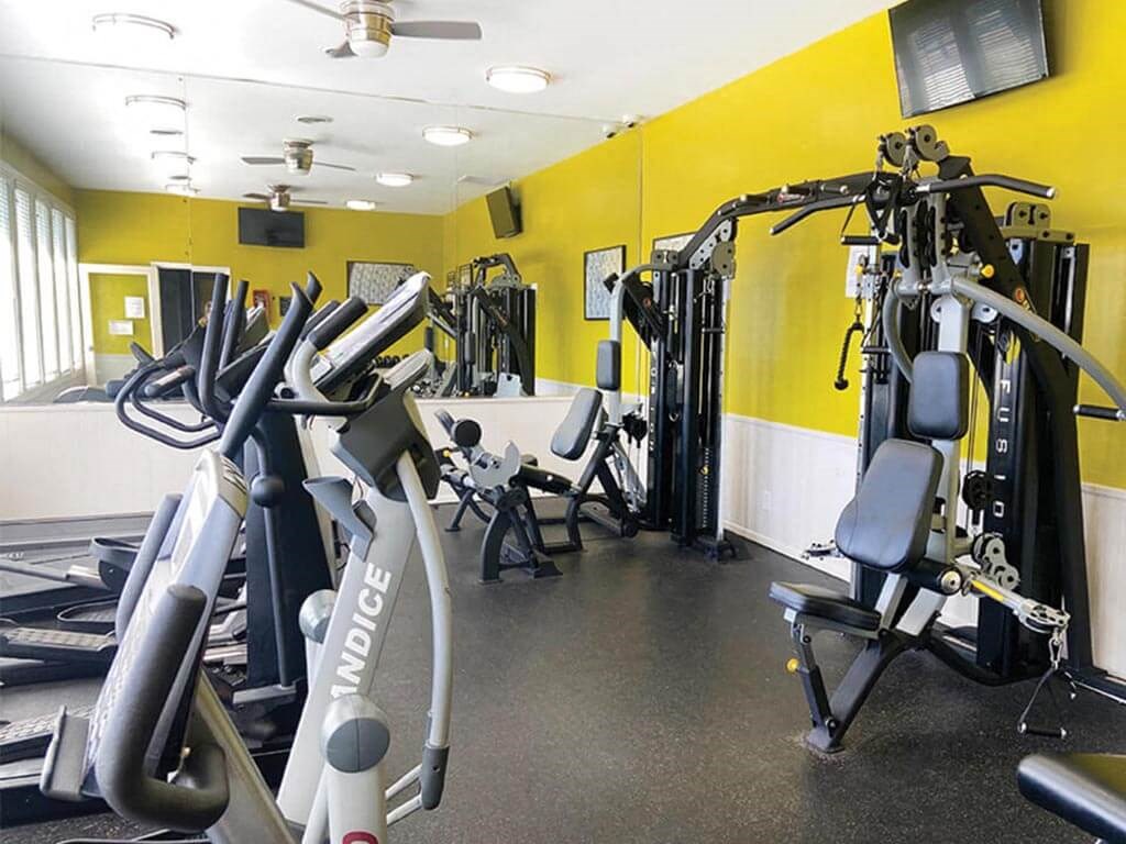 a gym with weights and cardio equipment in a yellow room