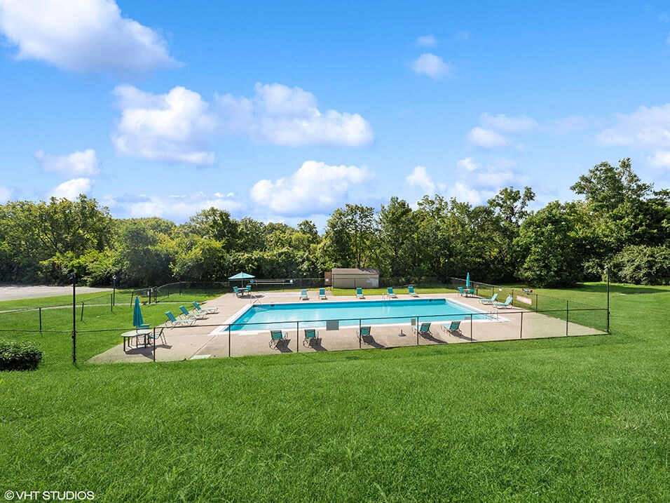 a swimming pool in the middle of a grass field with chairs around it