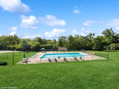 a swimming pool in the middle of a grass field with chairs around it