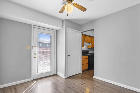 A room with a ceiling fan and a kitchenette in the other room.