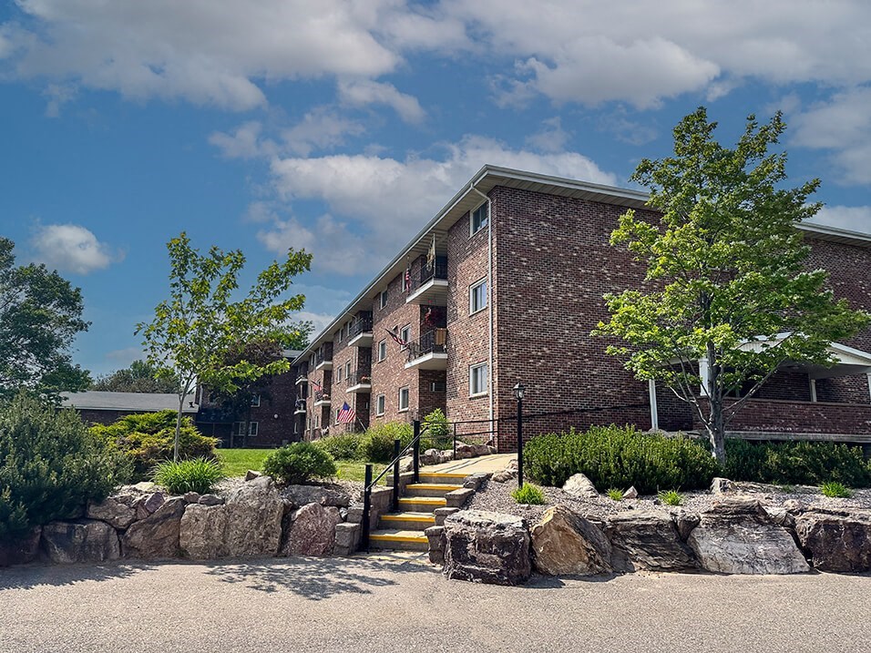 a brick apartment building with a stone retaining wall and landscaping