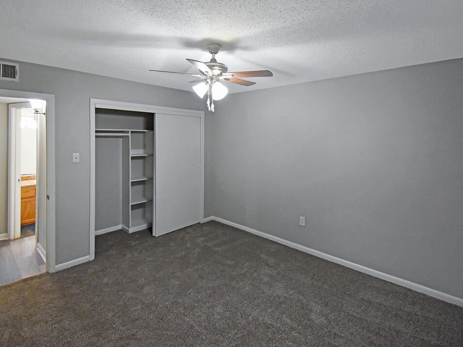 an empty living room with a ceiling fan and a closet