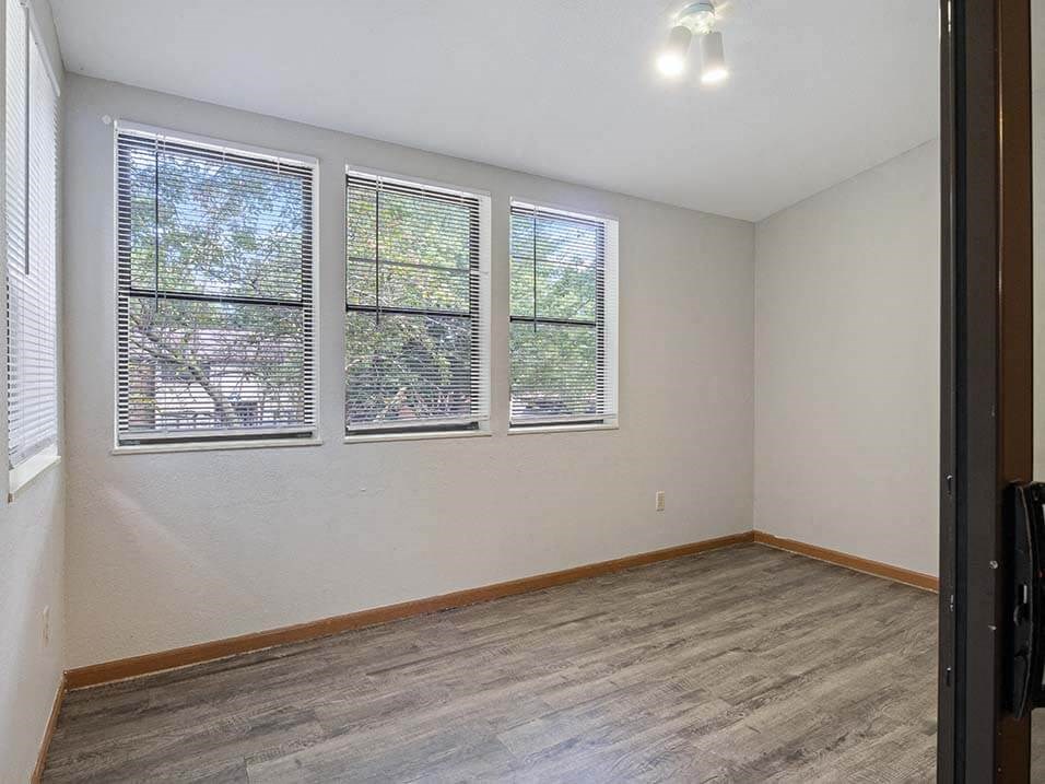 room in apartment with a wood floor and three windows