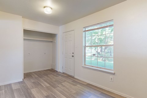 A room with a white door and a window with a view of trees.