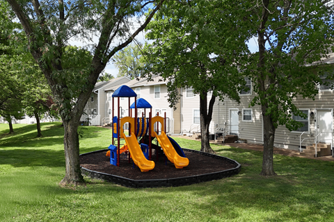 A playground with a blue and yellow slide in the middle of a grassy area.