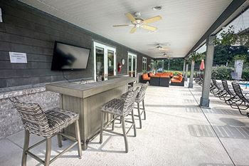 a patio with a bar and chairs and a television by the pool at woodland ridge apartments