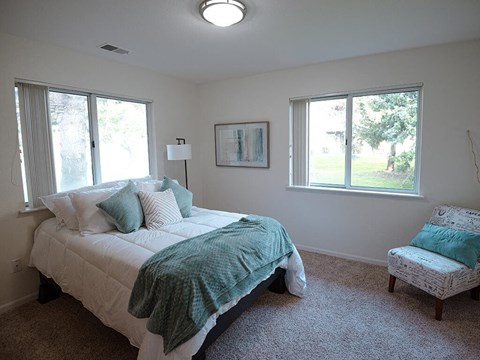 a bedroom with a bed and a chair and two windows