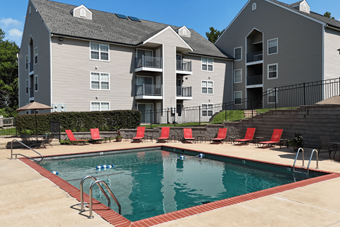 A swimming pool with red chairs and a building in the background.