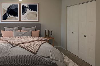 A bedroom with a bed, pillows, a blanket, and a painting on the wall.