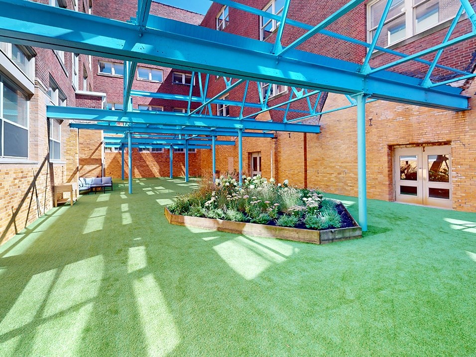 a patio with green grass and a flower bed in front of a brick building