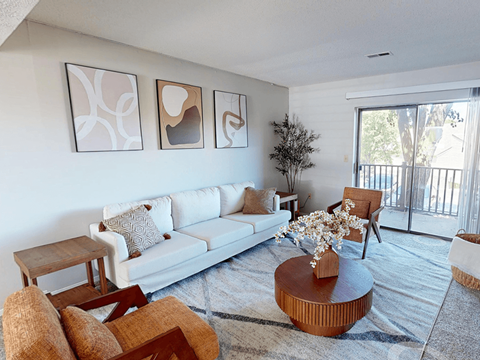 A living room with a white couch, a coffee table, and three abstract paintings on the wall.