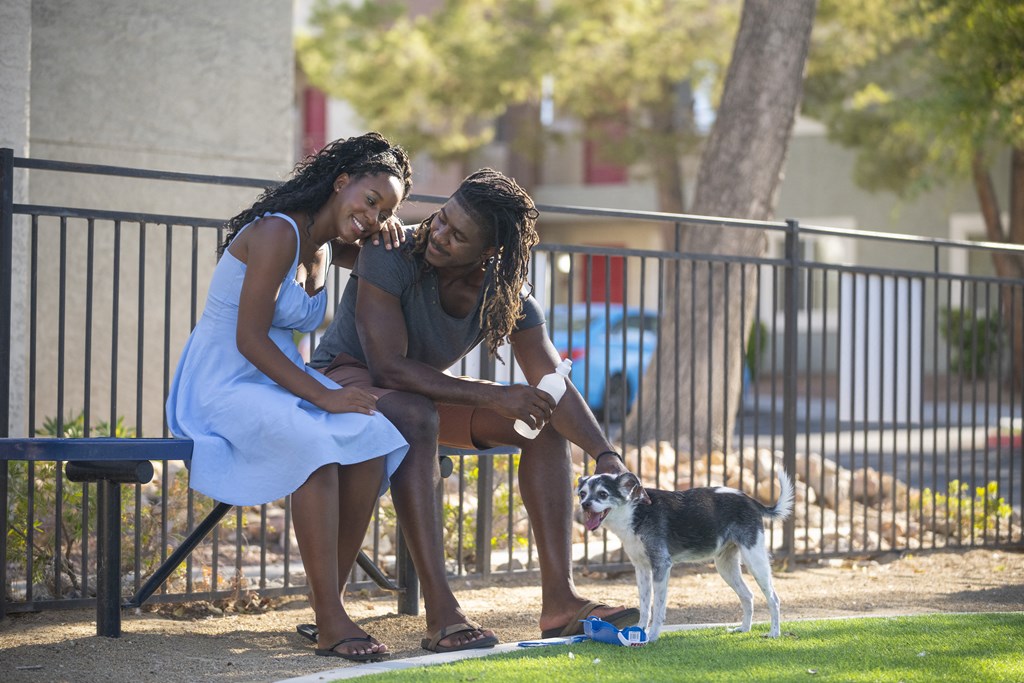 A man and woman sitting on a bench with a dog on the ground. at Solstice Apartment Homes, Nevada, 89108