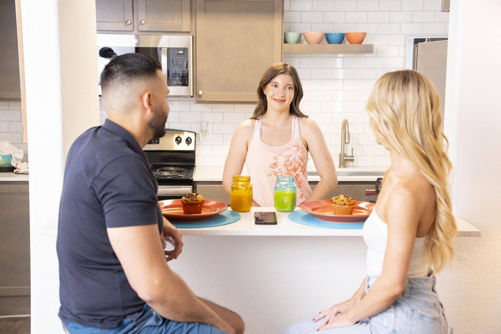 A man and two women are sitting at a kitchen island with food and drinks. at The 95 Apartments, Las Vegas, NV