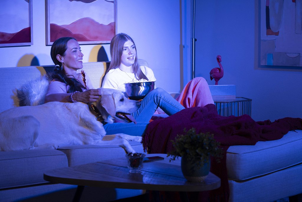 Two people sitting on a couch with a dog and watching TV. at The Neon Apartments, Nevada