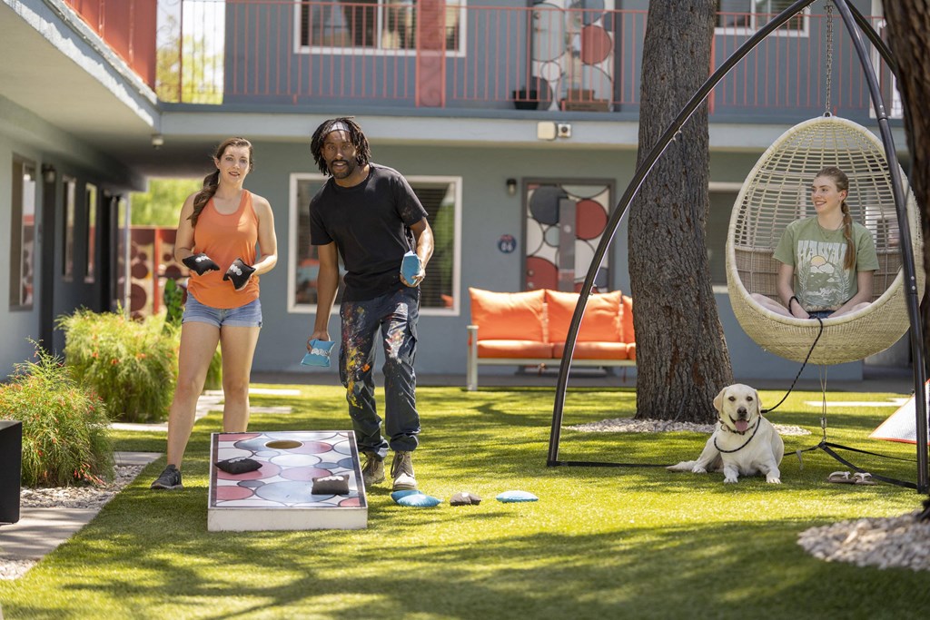 A man and a woman are playing a game on the lawn with a dog sitting under a hanging chair. at The Neon Apartments, Las Vegas