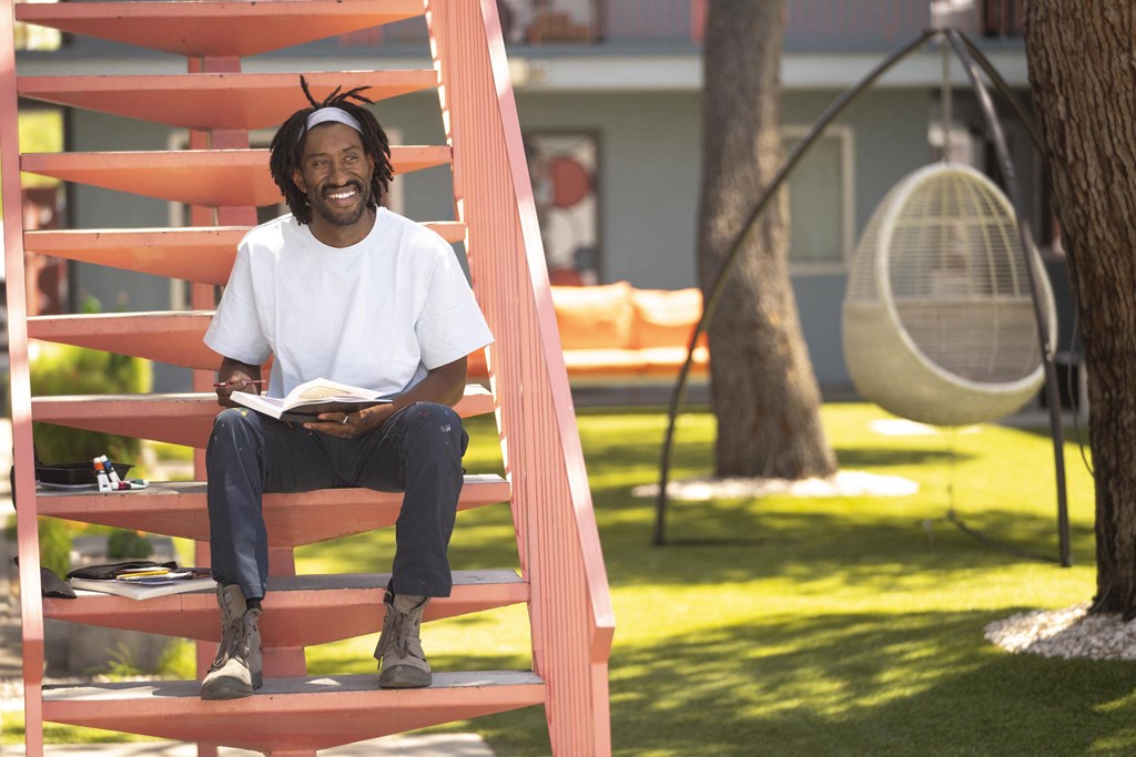 A man with dreadlocks is sitting on a red staircase reading a book. at The Neon Apartments, Las Vegas