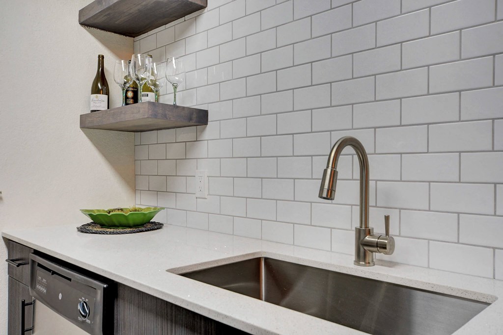 A kitchen with a white tiled wall and a stainless steel sink. at Namaste Apartments, Las Vegas