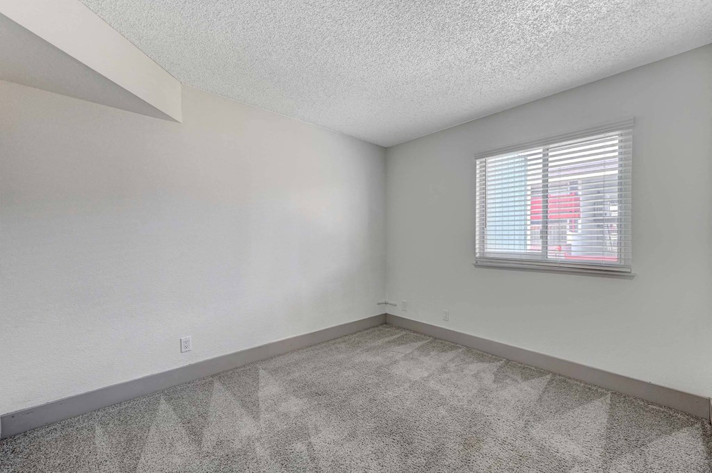 A room with a carpeted floor and a window with blinds. at Namaste Apartments, Las Vegas, 89102