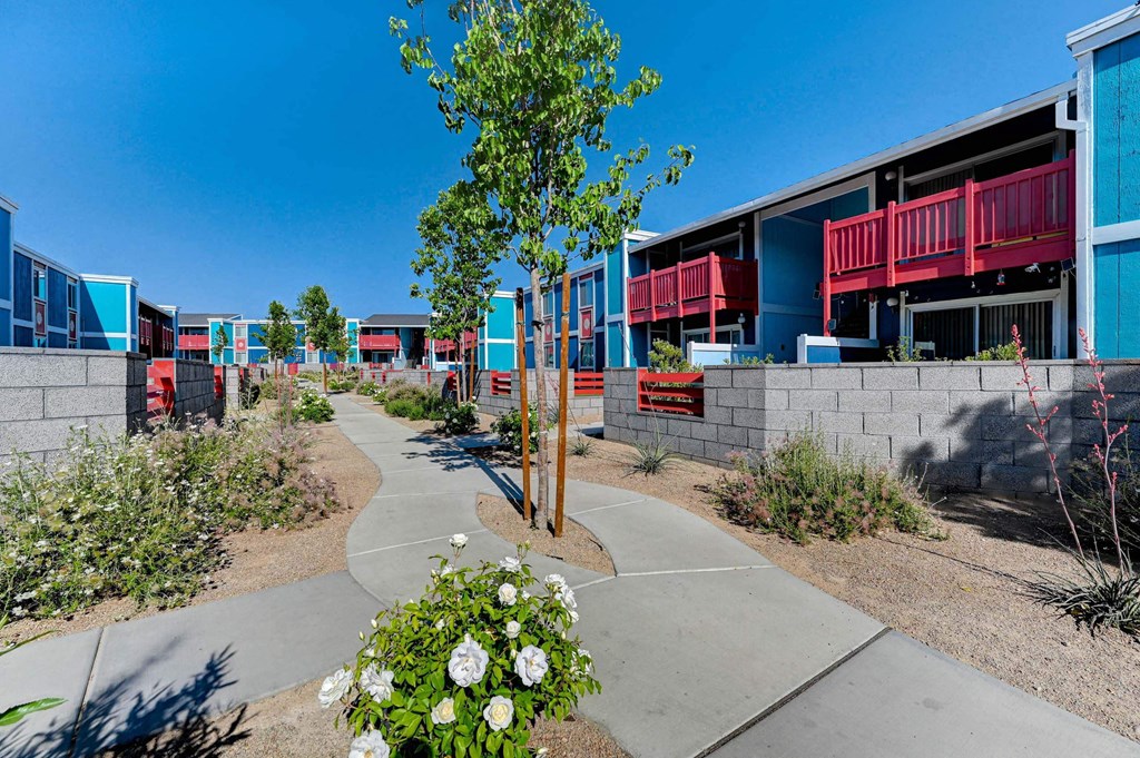 A tree with white flowers in the foreground and a building with red railings in the background. at Namaste Apartments, Las Vegas