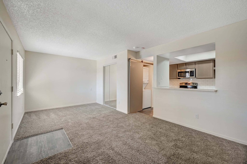 A spacious living room with a carpeted floor and a kitchen area at Solstice Apartment Homes, Las Vegas, NV, 89108