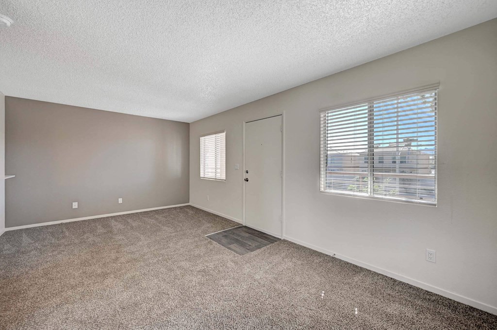 A room with a carpeted floor, a window with blinds, and a door. at Solstice Apartment Homes, Nevada