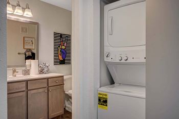 A washing machine is in a small bathroom with a mirror, toilet, and sink. at Solstice Apartment Homes, Las Vegas, Nevada