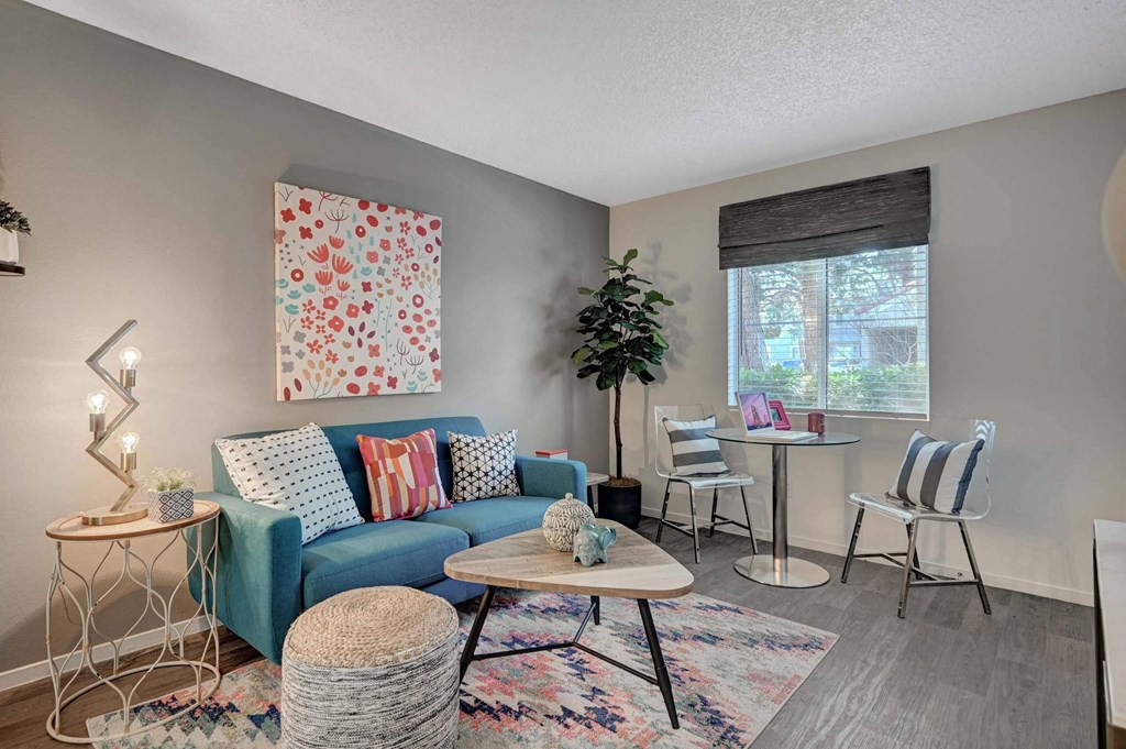 A living room with a blue couch, a white table, and a colorful rug. at Solstice Apartment Homes, Las Vegas, NV, 89108