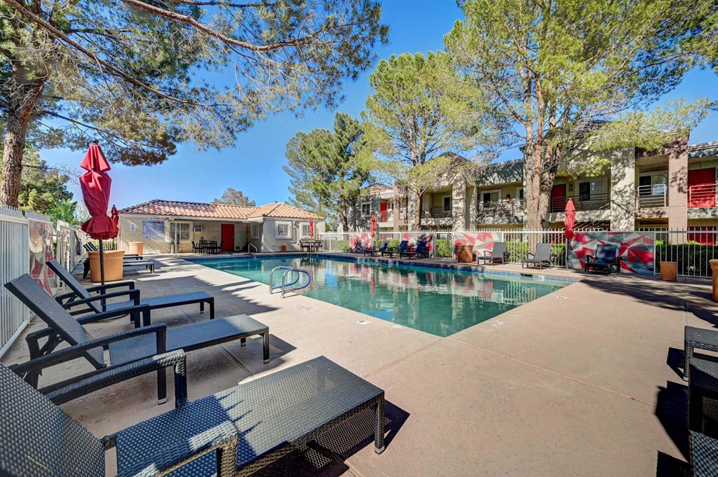 A pool area with lounge chairs and umbrellas. at Solstice Apartment Homes, Las Vegas, 89108