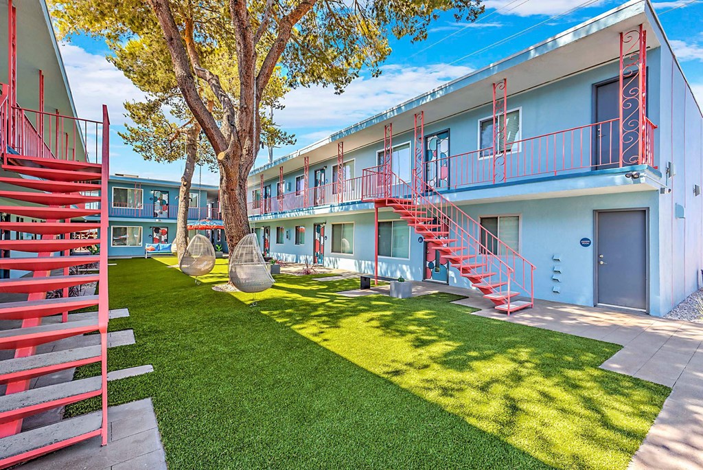 A tree in a courtyard with a red staircase. at The Neon Apartments, Las Vegas, NV