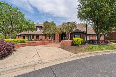 the front of a brick house with a driveway and trees
