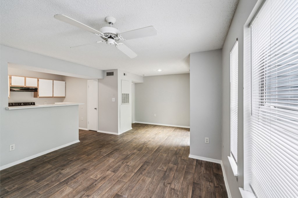 an empty living room with a ceiling fan and a kitchen