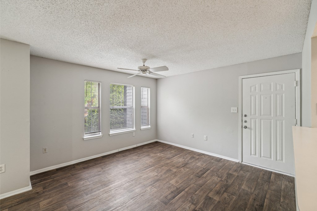 the spacious living room of an empty home with a ceiling fan