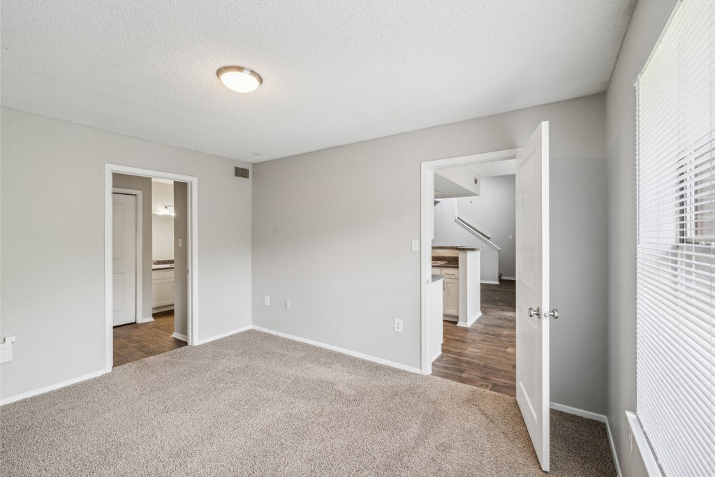 an empty living room with white blinds and a door to a hallway with a