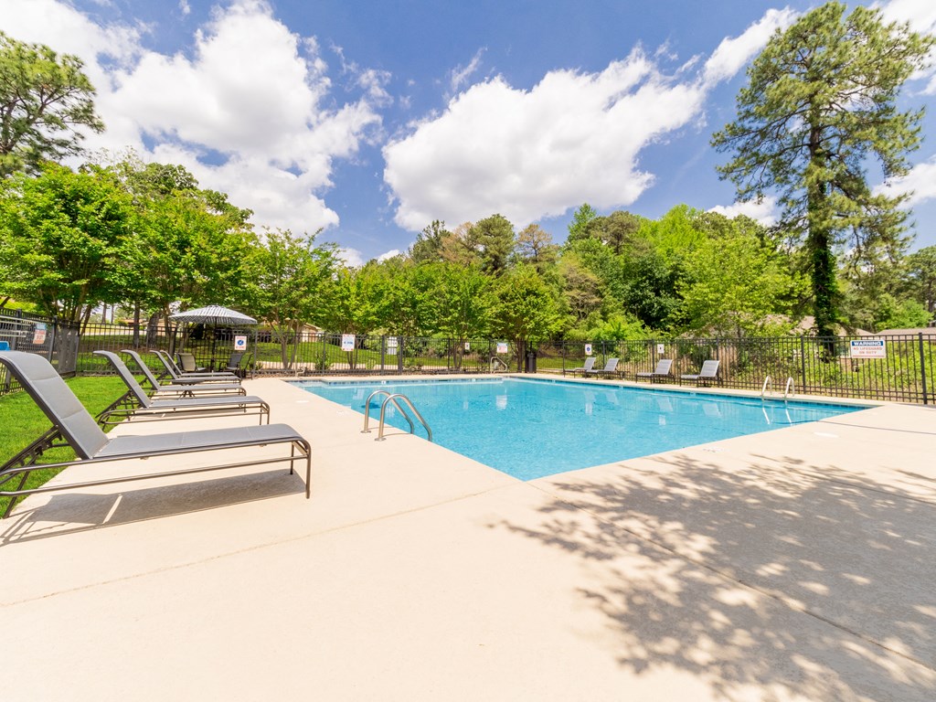 a swimming pool with chairs and trees in the background