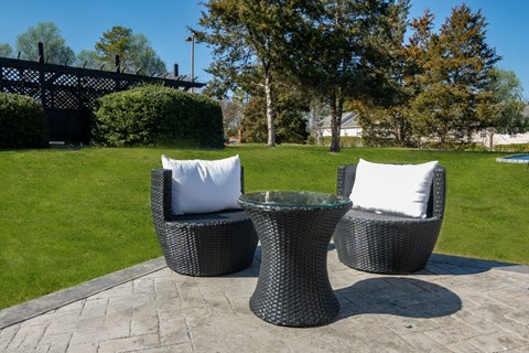 three chairs and a table with pillows on a stone patio