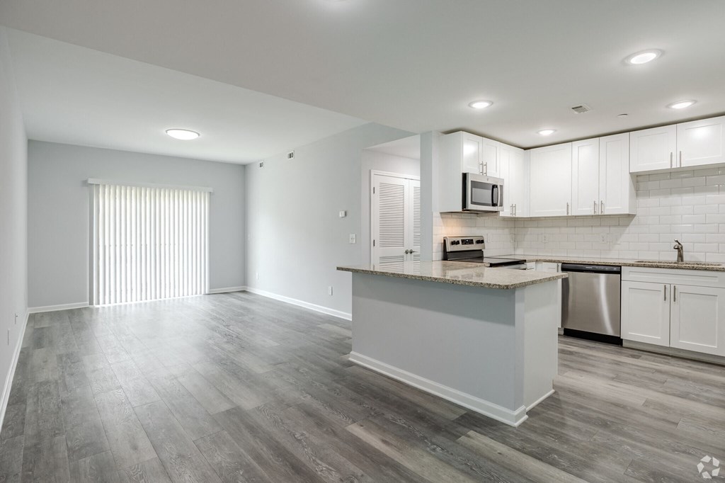 an empty kitchen and living room with white cabinets and stainless steel appliances