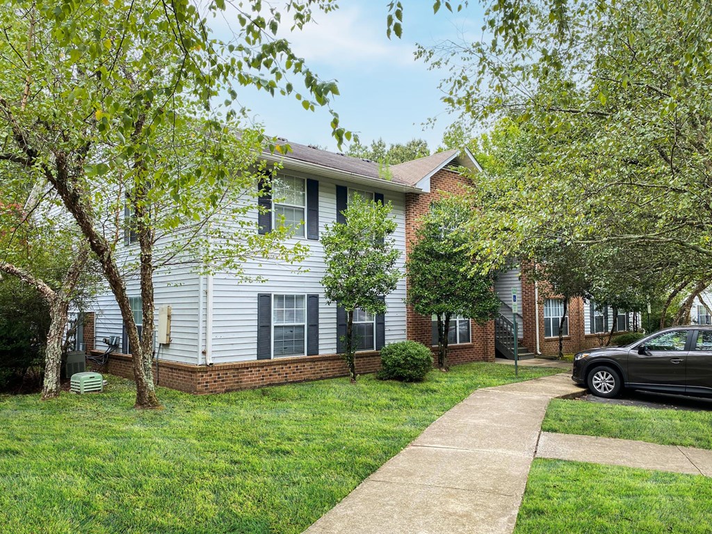 a white and brick house with trees and a sidewalk