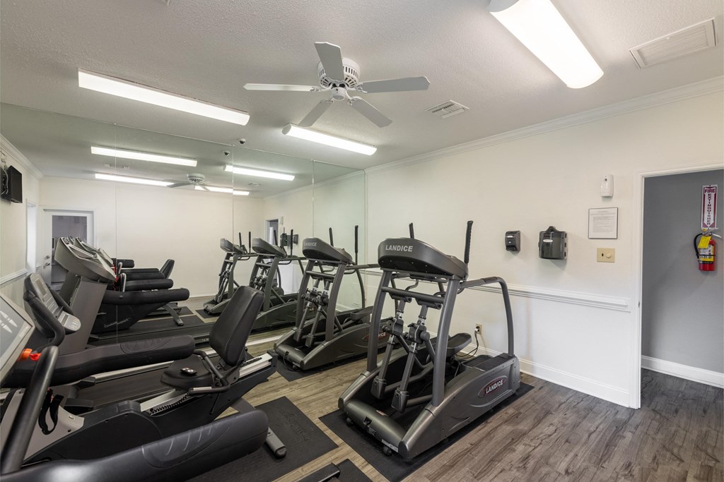 a gym with cardio machines and a ceiling fan